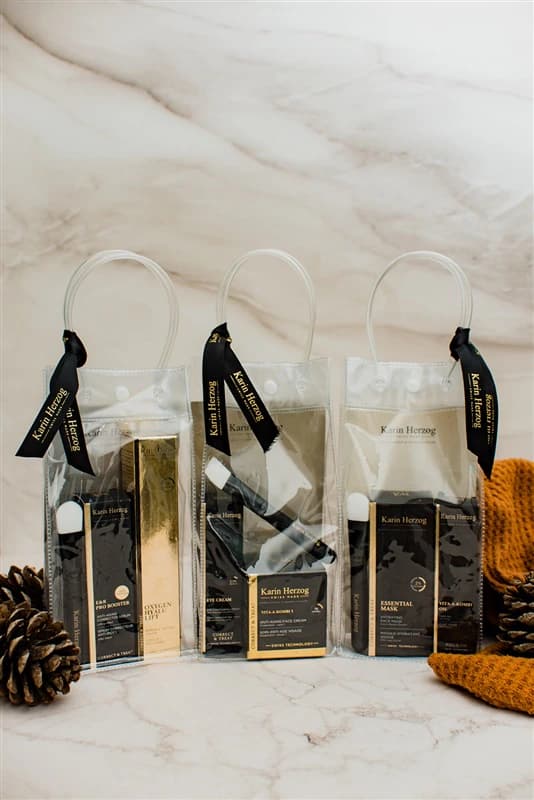Trois sachets cadeaux Karin Herzog à rubans noirs, posés sur du marbre
